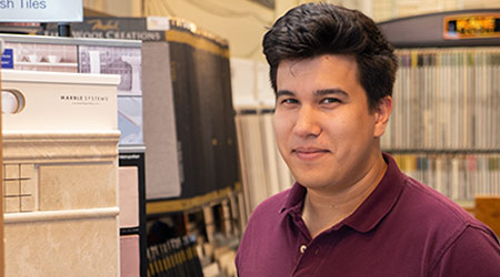 Alex Gim-Fain standing next to selection of tile flooring wearing maroon polo shirt